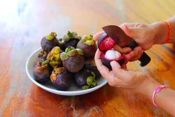 Close up of woman's hands cutting fresh mangosteens. Purple mangosteen as tropical fruit peeling with knife in women’s hands