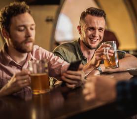 Cheerful friends drinking draft beer in a pub