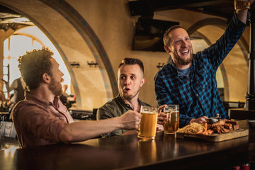 Friends drinking draft beer and watching tv in a pub