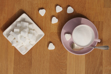loose sugar in a pink tea cup and saucer, refined slices, sugar tongs, heart-shaped candies, concept of excessive sugar consumption, diabetic, close-up, copy space, top view
