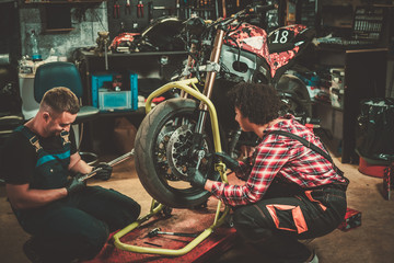 Fototapeta na wymiar Mechanic and his helper repairing a motorcycle in a workshop