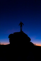 silhouette of man with open arms on top of a rock