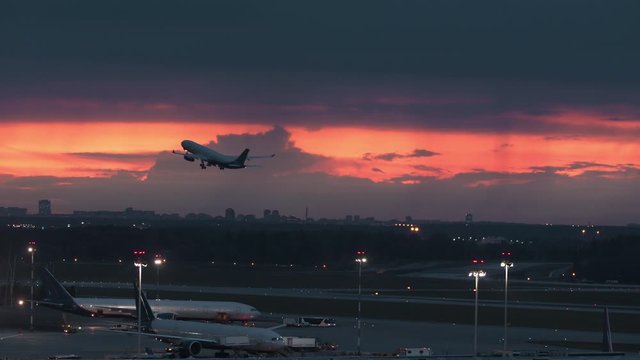 An early takeoff at an airport - a plane rises in the reddening sky, leaving two other planes below