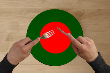 hands with cutlery on a plate with the state national flag of Bangladesh, copy space