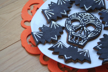 Halloween cookies in shape of skull and bat on a plate on wooden background. Halloween sweet food