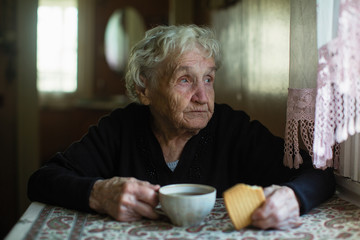 An elderly woman drinking tea with cookies at home. Taking care of lonely old pensioners.