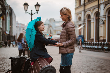 Obraz premium Little girl 6 years old child with an umbrella in rubber boots having fun with her mother on a bench in the center of Moscow in the fall or spring.