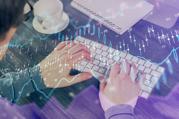 Double exposure of graph with man typing on computer in office on background. Concept of hard work.