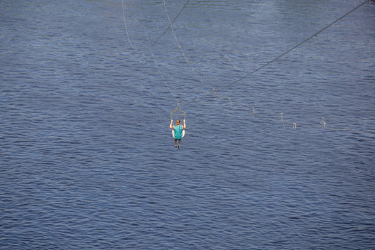 Rear view of young woman riding on zip line against a background of a blue river water wave, Kyiv, Ukrainee