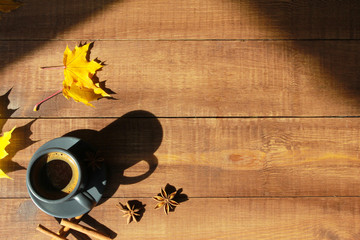 Grey cup of coffee, cinnamon, yellow maple leaves on dark wooden table. Autumn background concept....