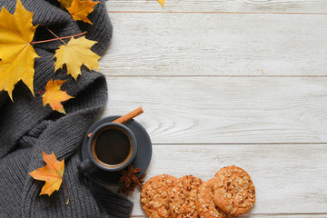 Grey cup of coffee, cookie, yellow fall leaves, scarf  on white wooden table. Autumn background concept. Fall menu, expresso, coffee shop, dessert, copy space