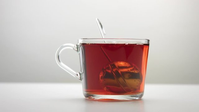 a tea infuser spoon moves in slow motion into a transparent tea cup