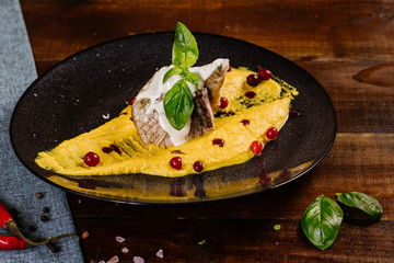 A dish with white fish and yellow sauce on the wooden background