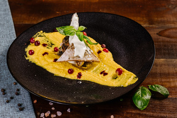 A dish with white fish and yellow sauce on the wooden background