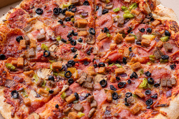 Delicious Italian pizza with bacon, olives, sausages and mushrooms. Top view. Fresh tasty pizza in cardboard box - close-up.