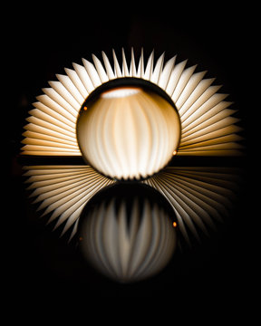abstract glassball on a reflective surface and a light admitting book in the background during night