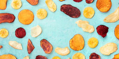 A panorama of dry fruit and vegetable chips, healthy vegan snack, an organic food flat lay on a blue background, forming a frame with a place for text