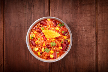 Chili con carne, overhead shot on a dark rustic wooden background with a nacho chip