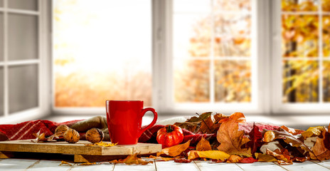 Autumn desk with mug and blurred fall window space 