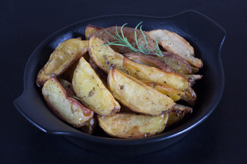Close up rustic roasted potatoes with rosemary branch on black plate on black background
