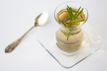 Rosemary tea in Armudu glass with branch of rosemary in it and spoon on the table on white background