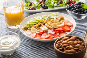 Healthy breakfast served with plate of yogurt muesli kiwi strawberries and banana