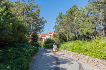 Fototapeta na wymiar Woman view from behind walks along the path of a quiet Park in Porto Rotondo Sardinia on a clear day