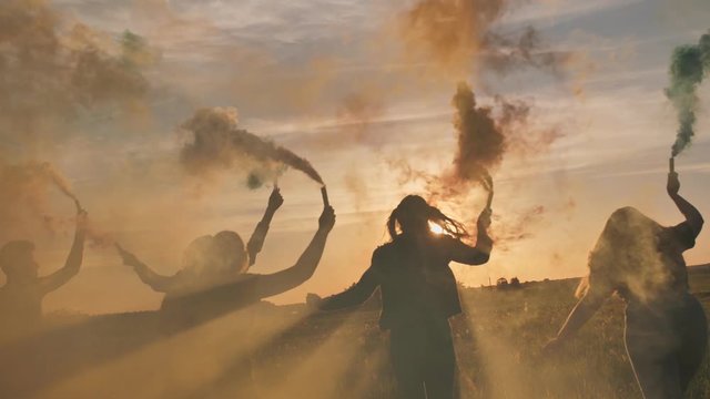 Happy friends waving colorful smoke at sunset.
