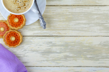 Cup of coffee and sweet cookies with orange jelly. Composition with Cup of coffee and sweet cookie glazed with jelly flavored orange on wooden kitchen table with copy space. Concept lifestyle and food