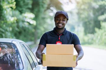 Smile african male postal delivery courier man in front of car delivering package.