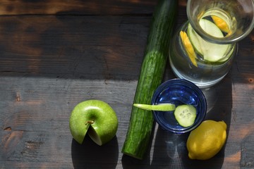 Fresh water made with cucumber, apple and lemon on a burned wood background
