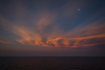 Moon rising over the sea and beautiful orange-colored clouds after sunset