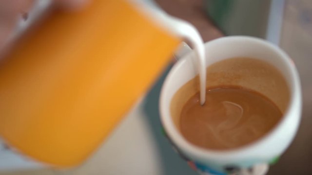 barista adds milk to cappuccino in cup and makes image