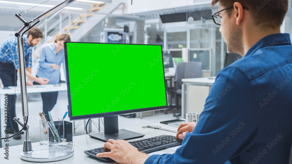 Aufkleber Over the Shoulder Shot of Engineer Working with Green Mock-up Screen Desktop Computer. In the Background Engineering Facility with Specialists Working on Blueprints and Drawings with Industrial Design