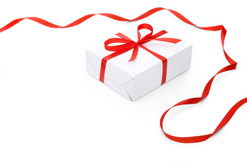 Perfect white gift box tied with a bright red satin ribbon with a bow and a red ribbon curved in the corner of the picture isolated on white background