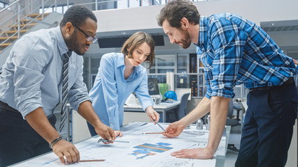 In the Industrial Engineering Facility: Female Designer Works with Industrial Engineer and Master Technician, They have Discussion, Analyse Engine Design Technical Drafts that are Lying on the Table