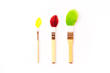 Three small children's brushes for artwork with multi-colored painted feathers imitating paint. Minimalistic creative concept.