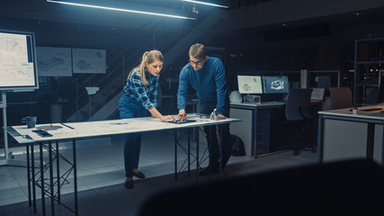 Industrial Design Engineering Facility Male and Female Engineers Work on a Blueprints and Technical Drawings Using Conference Table. Facility is Full of Computers with Screens Showing Engine Concepts
