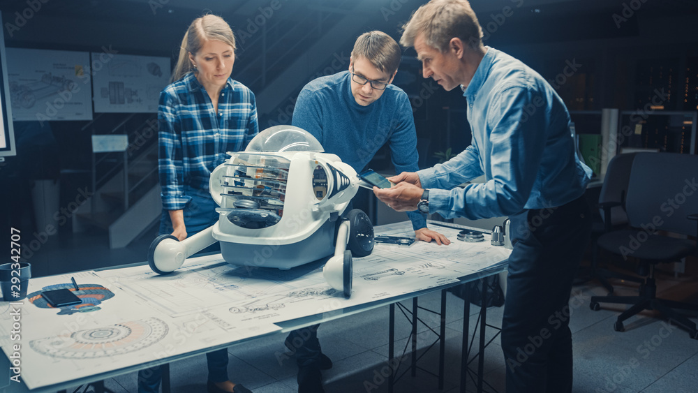 Leinwandbilder robotics engineering facility three technical engineers talk and work on a wheeled robot prototype. 