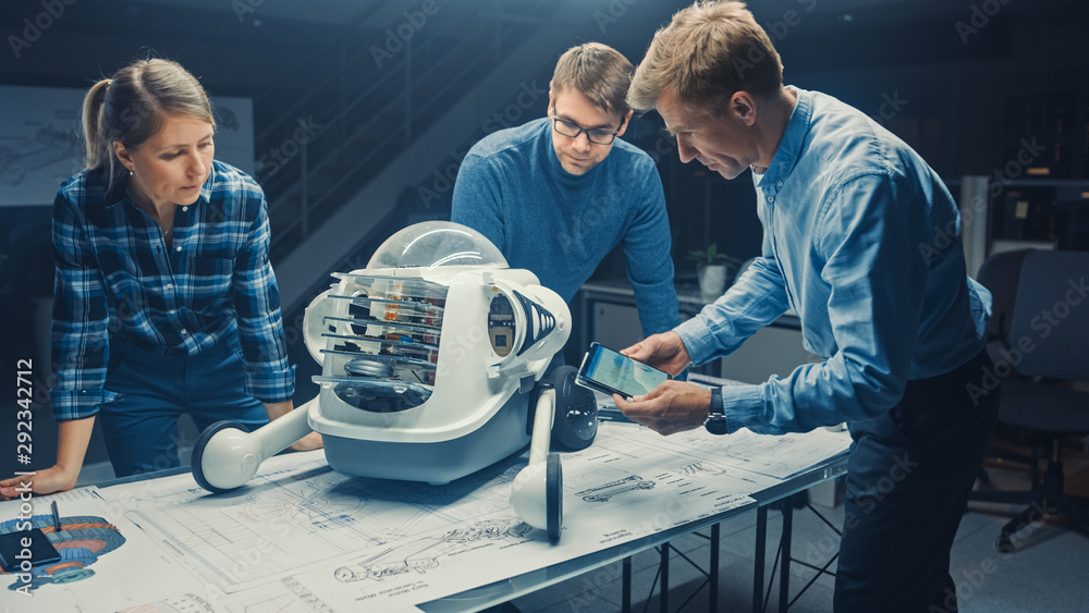 Leinwandbilder Robotics Engineering Facility Three Technical Engineers Talk and Work on a Wheeled Robot Prototype. In the Background High Tech Research Center with Screens Showing Industrial Design.