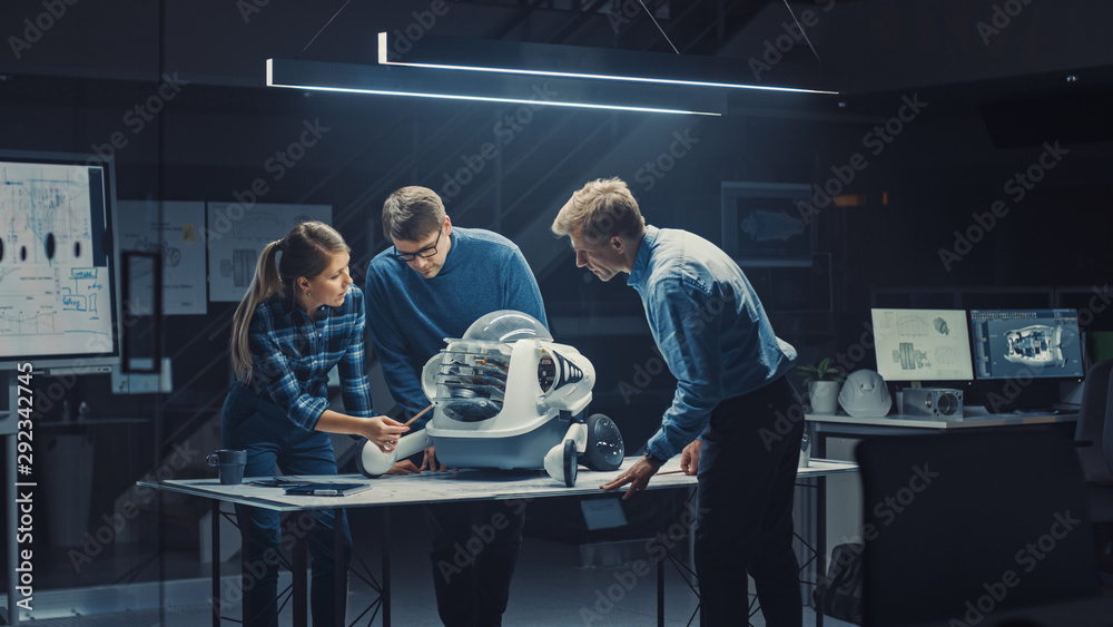 Fototapete Late at Night in Robotics Engineering Facility Three Technical Engineers Talk and Work on a Wheeled Robot Prototype. In the Background High Tech Research Center with Screens Showing Industrial Design
