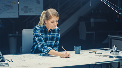 Female Engineer Sitting at Her Desk Works with Blueprints Laying on a Table, Uses Pencil, Ruler and...