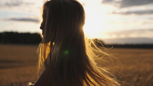 Close up of joyful smiling girl jumping against the blurred background of barley field at sunset. Happy laughing kid with blonde hair having fun at the wheat meadow with sunlight background. Slow mo