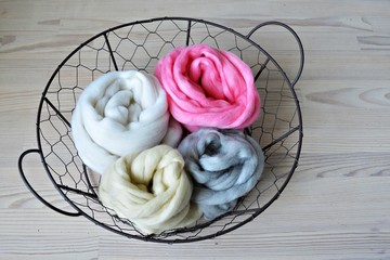 Grey, pink, vanilla and white merino wool in round wire basket on wooden table	