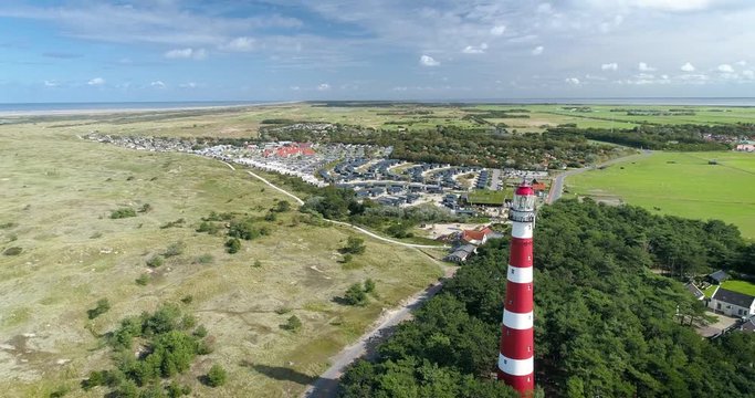 The Dutch Island Ameland with Red and White Striped Lighthouse, The Netherlands. Also in shot: Hollum, trees, dunes, North sea, blue sky, clouds. 4K Drone Footage.