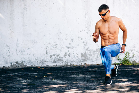 Horizontal image of young runner fit man stretching before exercises outdoors against concrete wall. Athlete male stretches after workout outside. Sport and people concept. Copy space for your text