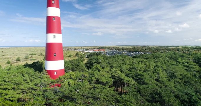 The Dutch Island Ameland with Red and White Striped Lighthouse, The Netherlands. Also in shot: Hollum, trees, dunes, North sea, blue sky, clouds, birds. 4K Drone Footage.