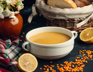 Lentil soup served in white bowl with lemons and bread