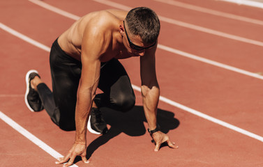 Shirtless sportsman preparing for running on racetrack at stadium. Male runner sprinting during training session for competition. People, sport and healthy lifestyle