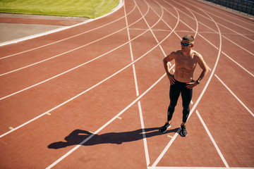 Above view image of young athlete man posing on racetrack at stadium. Professional shirtless sportsman during training session. People, sport and healthy lifestyle
